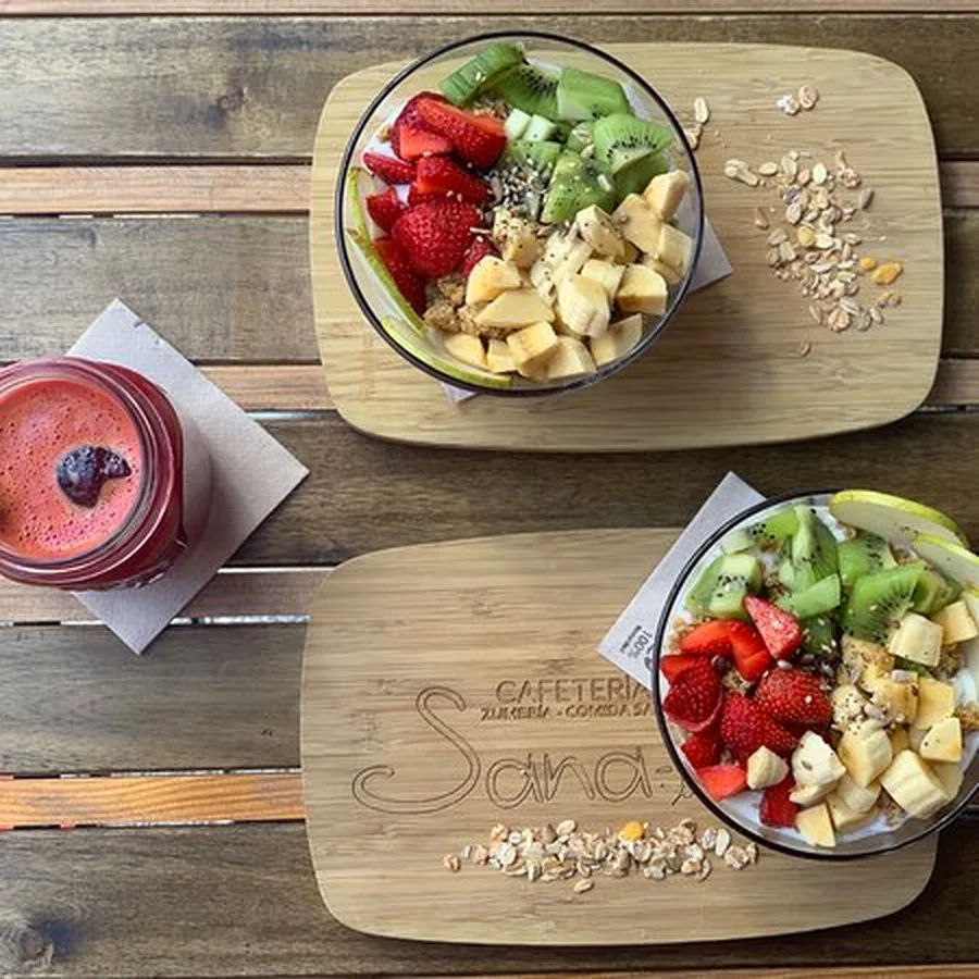 Dos bowls de yogur con fresa, kiwi, plátano y muesli sobre tablas de madera grabadas