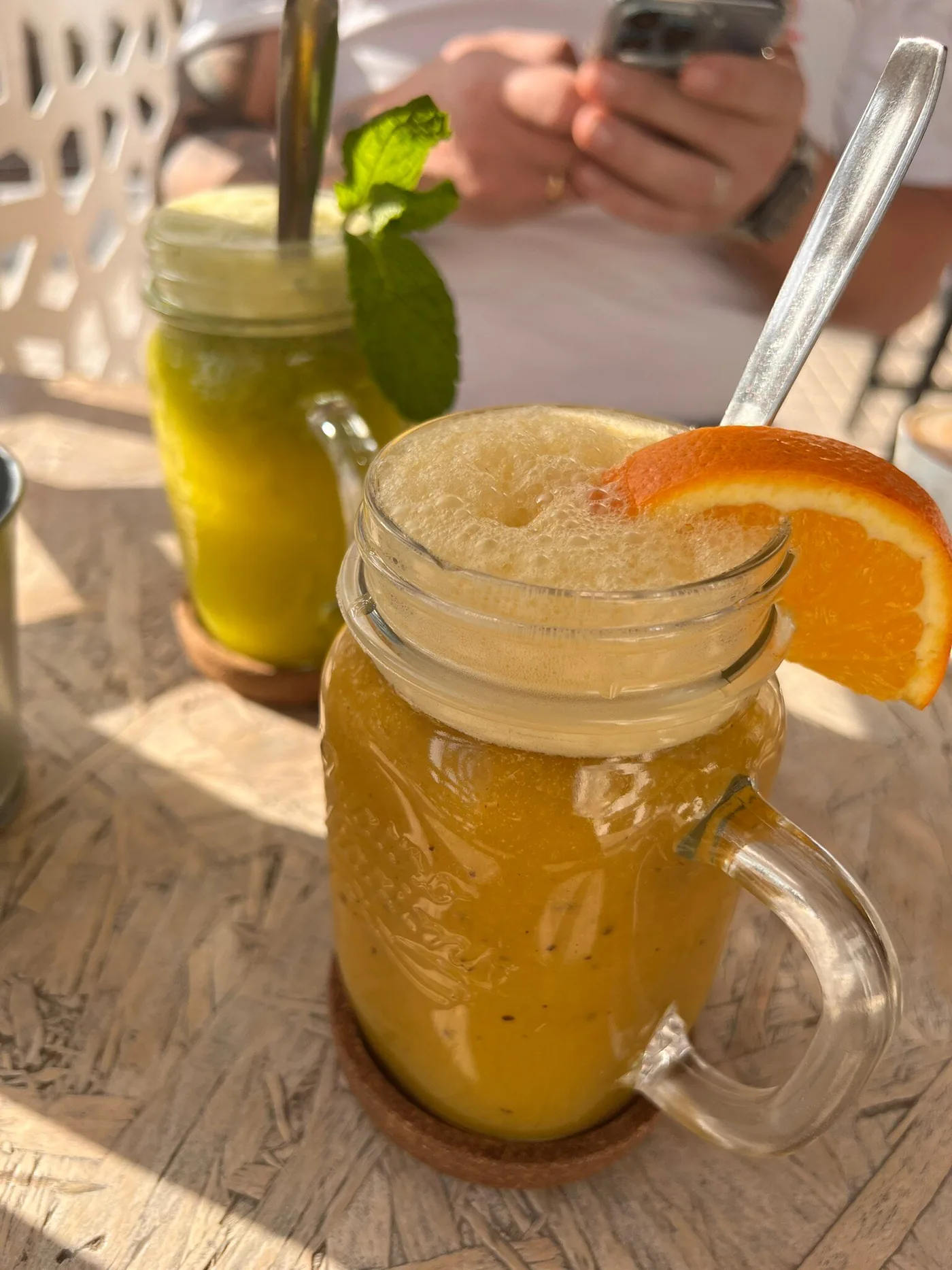 Zumo natural de naranja con rodaja de naranja y otro de menta al sol en la terraza